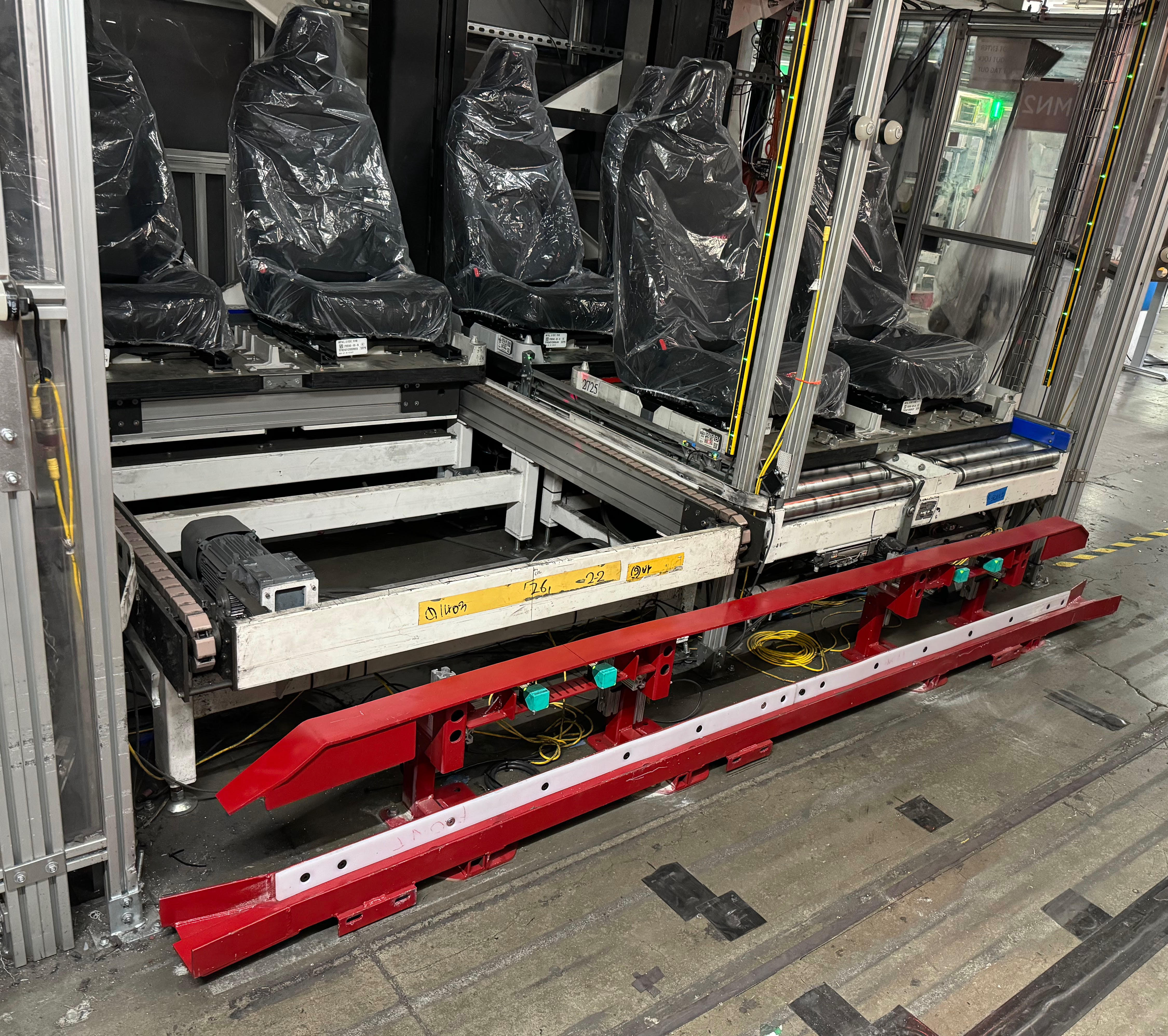 Red and white powder-coated AGV guide rails staged next to a seat-carrier conveyor on the Tesla assembly line.